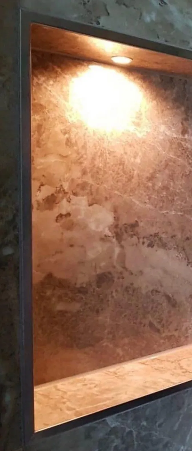 Belyst nisch i duschväggen med varmt ljus över stenmönstrade plattor
